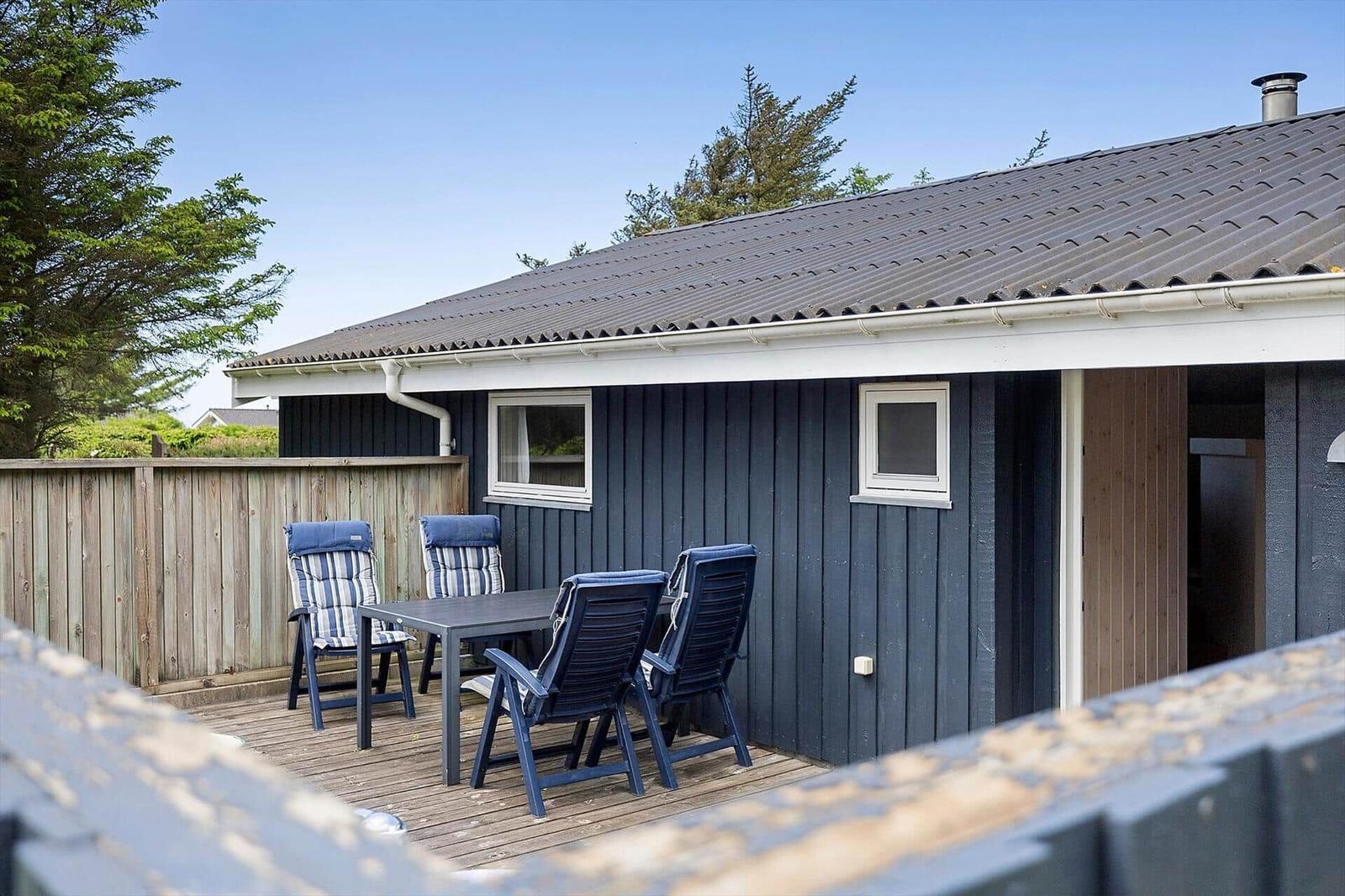 Terrasse mit Tisch und Stühlen vor einem blauen Holzhaus mit Dach und Fenstern.