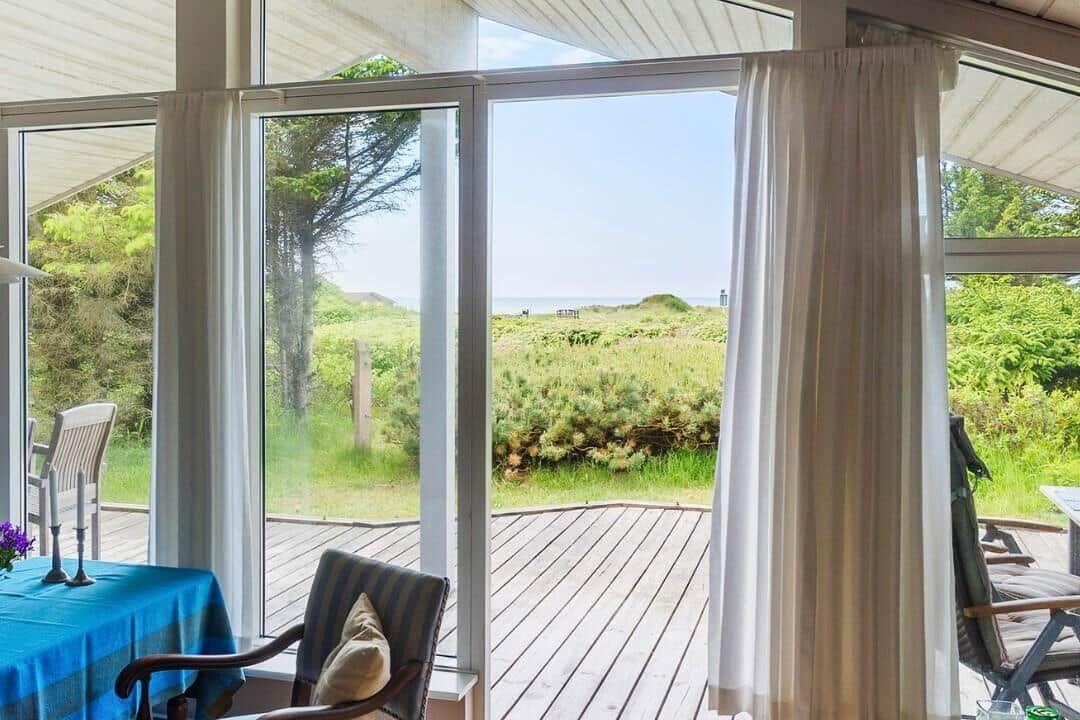 Durch große Fenster Blick auf eine Terrasse und Grünland bis zum Meer.