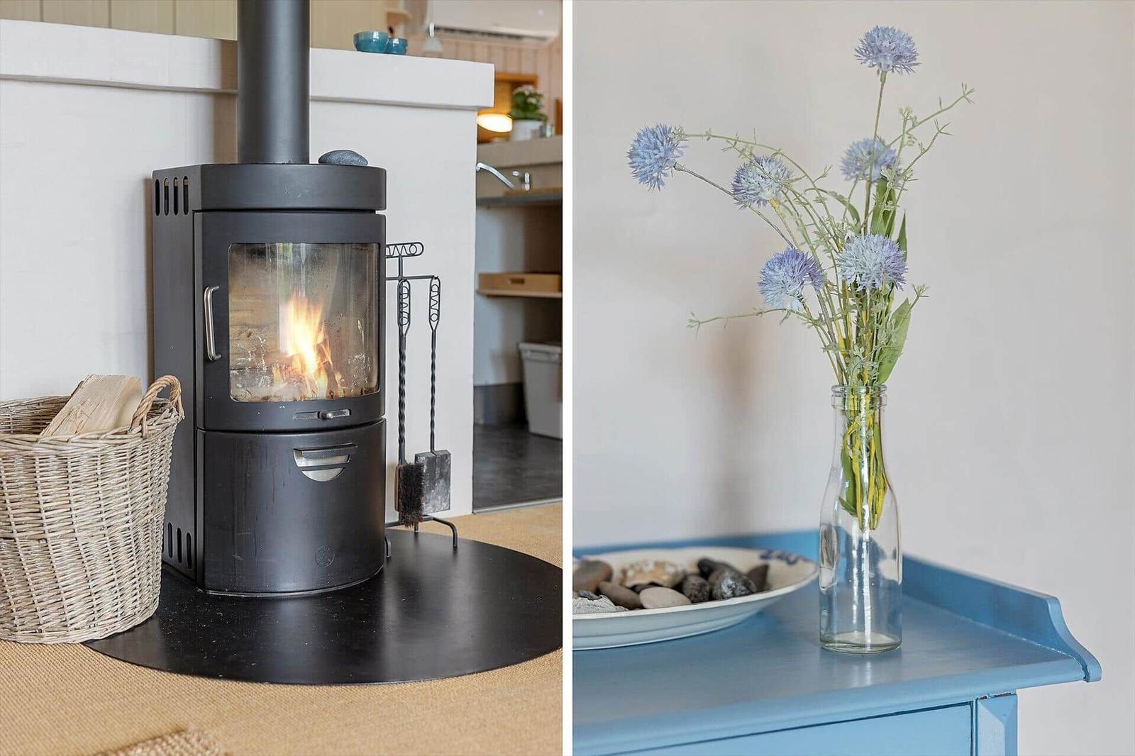 Kaminofen mit Holz und Blumen in Glasflasche auf blauem Tisch.
