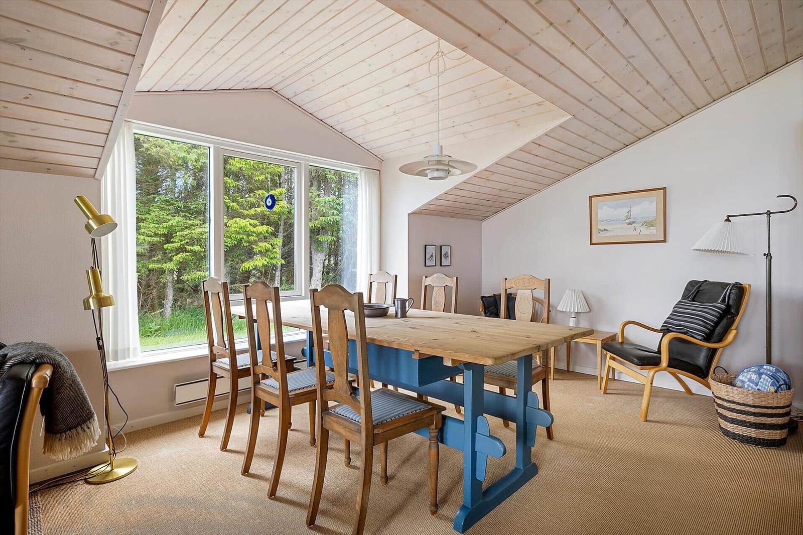 Esszimmer mit Holztisch, Stühlen und großem Fenster mit Blick auf Wald.
