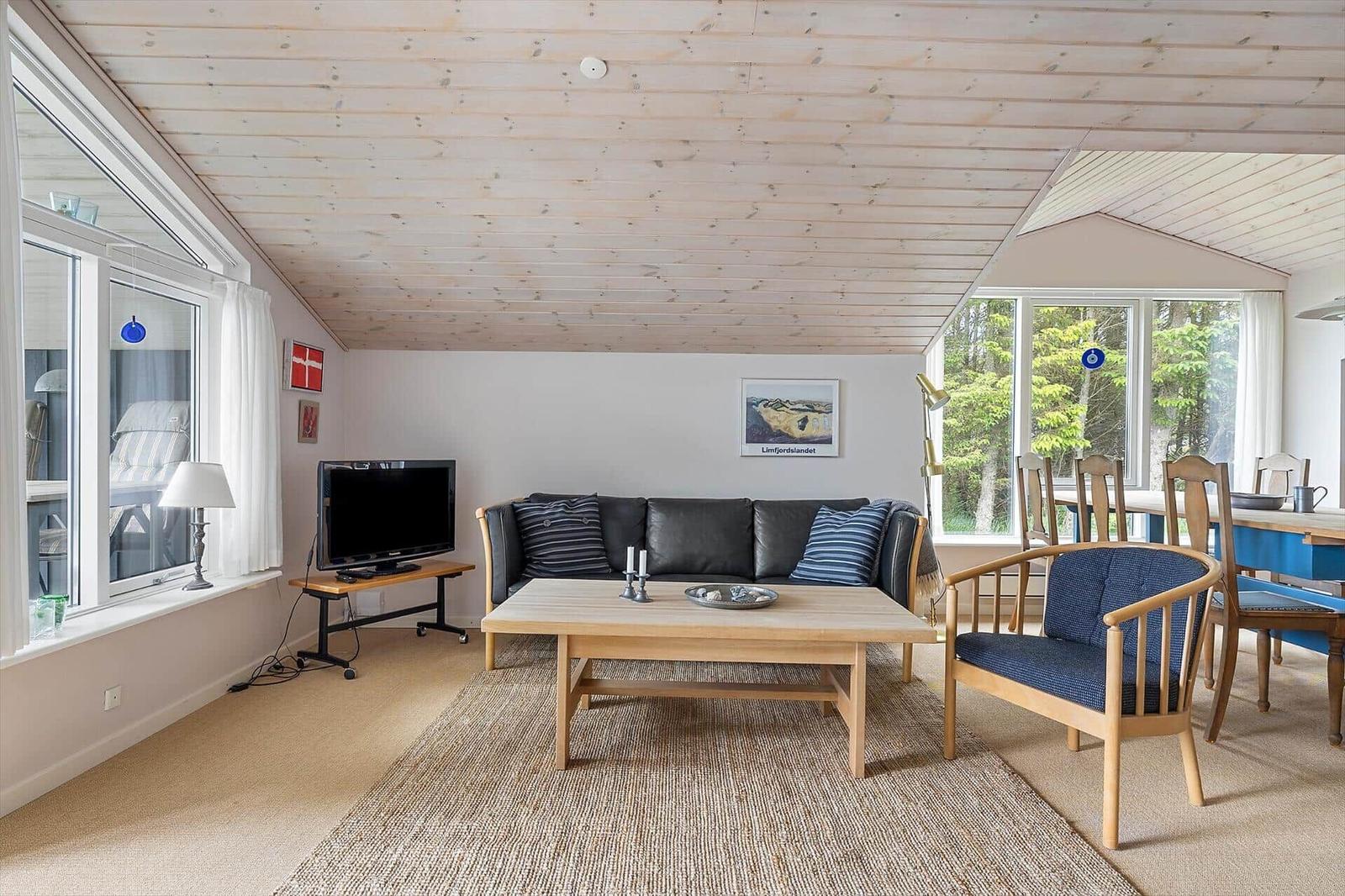 Wohnzimmer mit Sofa, Tisch und Stühlen. Holzdecke und große Fenster.