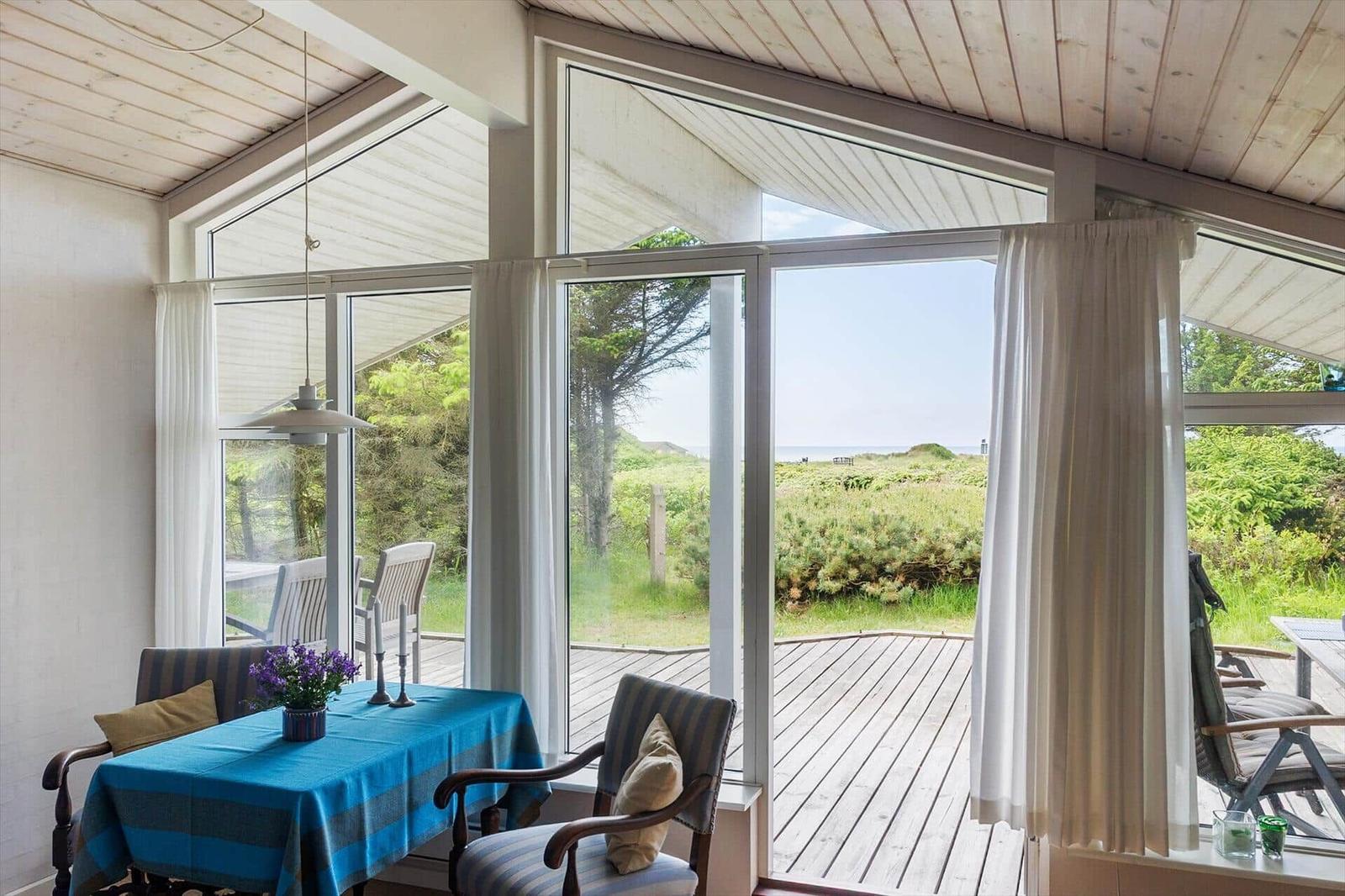 Ein Essbereich mit Tisch und Stühlen. Durch große Fenster sieht man einen Holzdeckenbereich und Grünland.