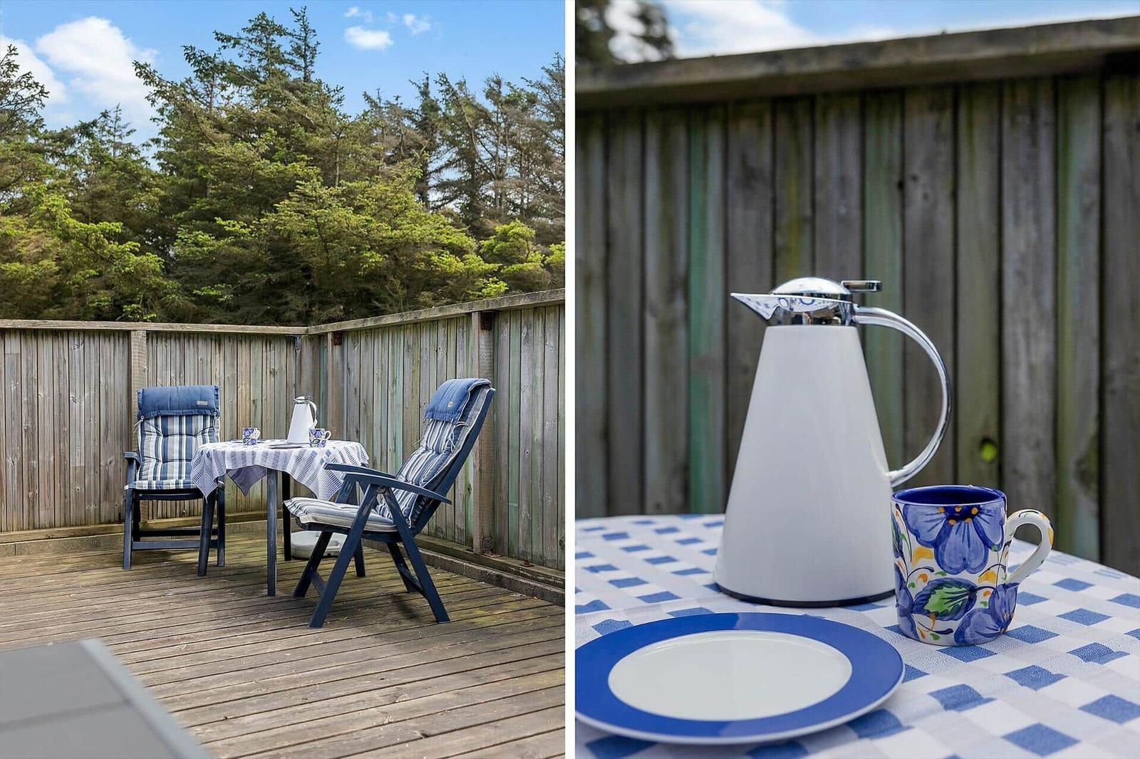 Terrasse mit Tisch, zwei Stühlen und Holzgeländer. Tisch mit Tischdecke und Geschirr.