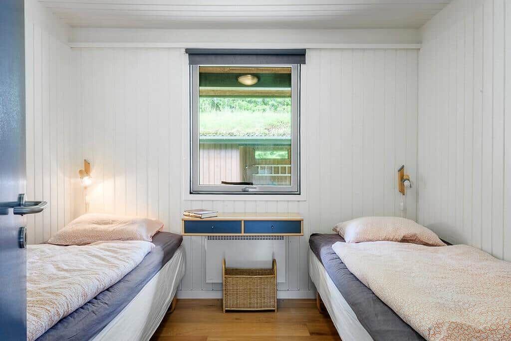 Two single beds in a room with wooden floor and white wall paneling. A window and a desk are visible.