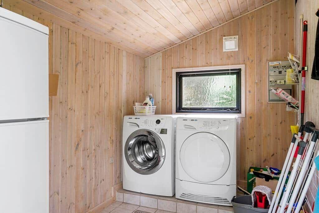Washing machine and dryer in wooden room with window and refrigerator.