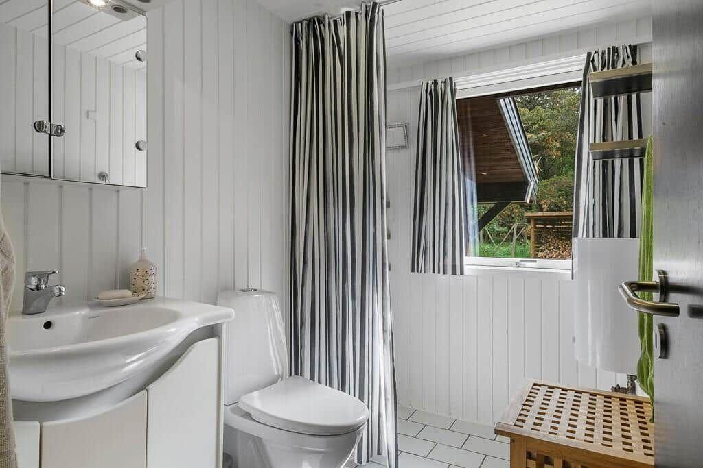 Bathroom with sink, toilet, shower, and window overlooking outdoor area.
