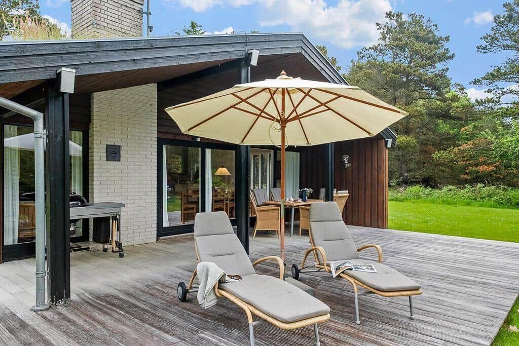 Deck with lounge chairs and umbrella in front of modern house with garden.