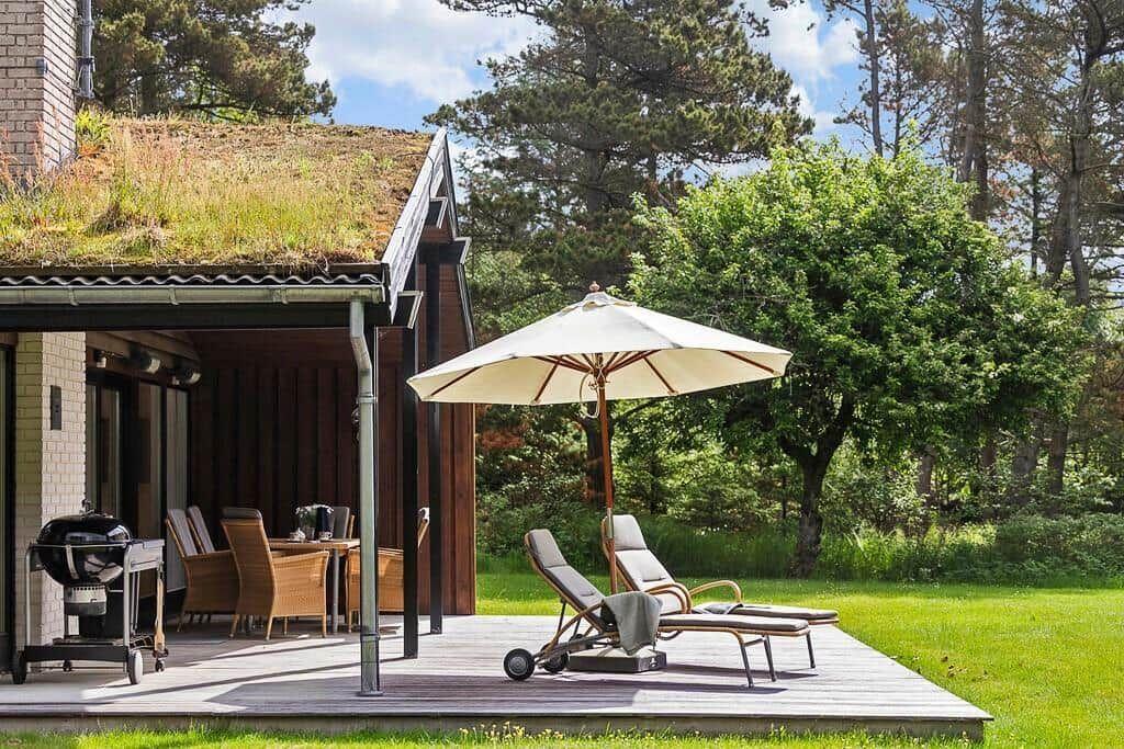 Deck with lounge chairs, umbrella, and grill. Lawn and trees in the background.