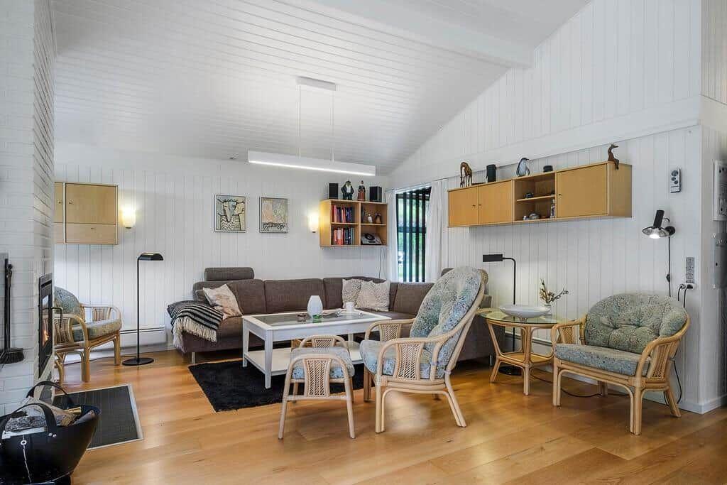 Living room with sofa, chairs, and wooden floor. Wall shelves and fireplace visible.