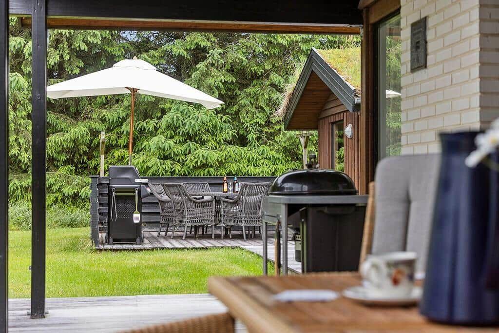 Deck with grill, table and chairs under a white umbrella.