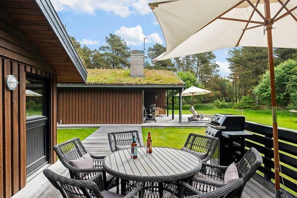 Deck with table, chairs, and grill. Lawn and forest in the background.