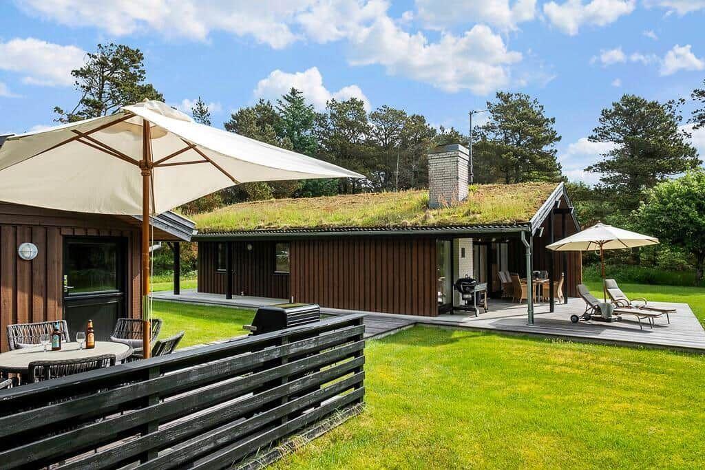 House with grass roof, terrace, sun loungers, and grill area in green surroundings.