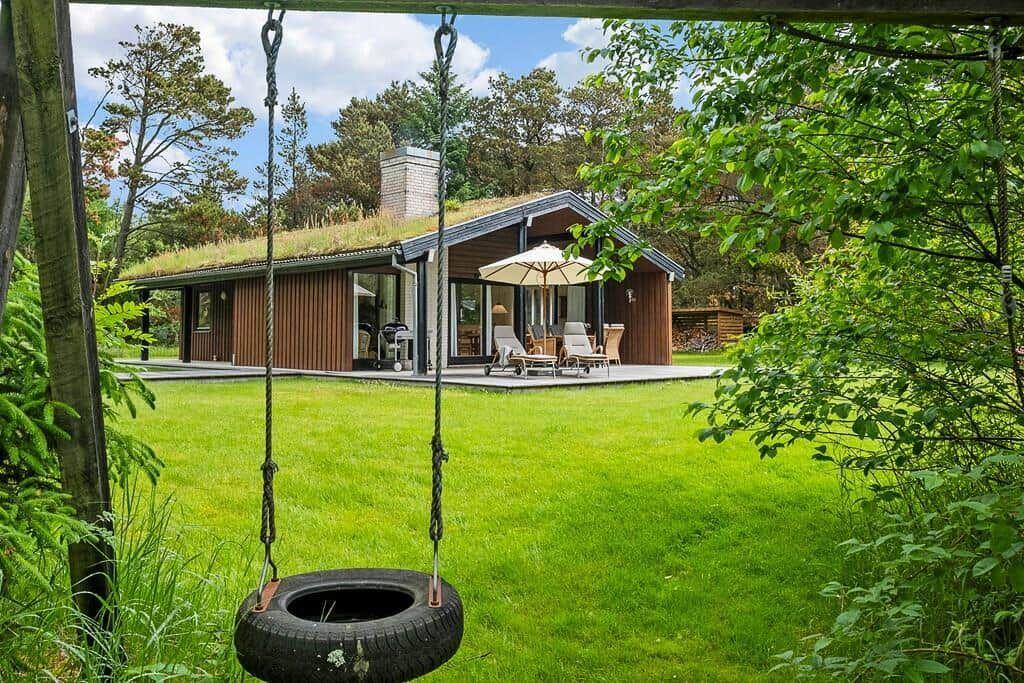 House with grass roof, terrace, and garden. A tire swing hangs in the foreground.