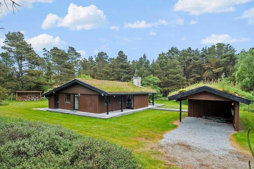 Modern wooden cabin with green roof and garage in the woods.