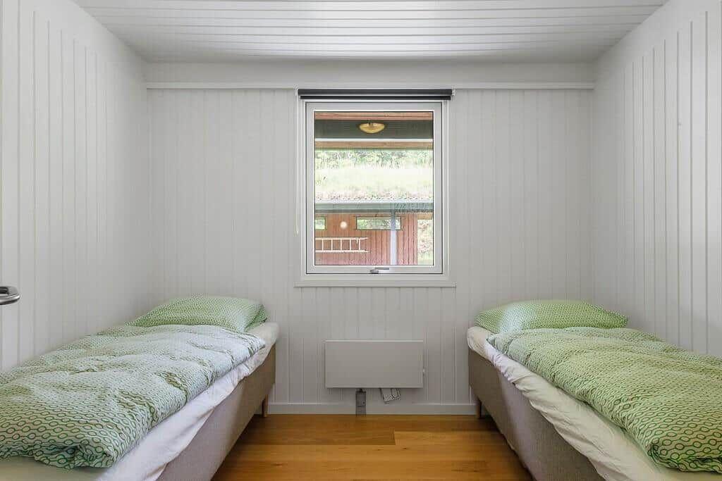 Two single beds with green bed linen are in a room with wooden floor and window.