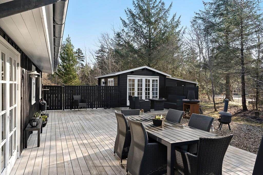 Terrasse mit Tisch und Stühlen, Grill und Sitzgelegenheiten vor einem Holzhaus in Waldnähe.