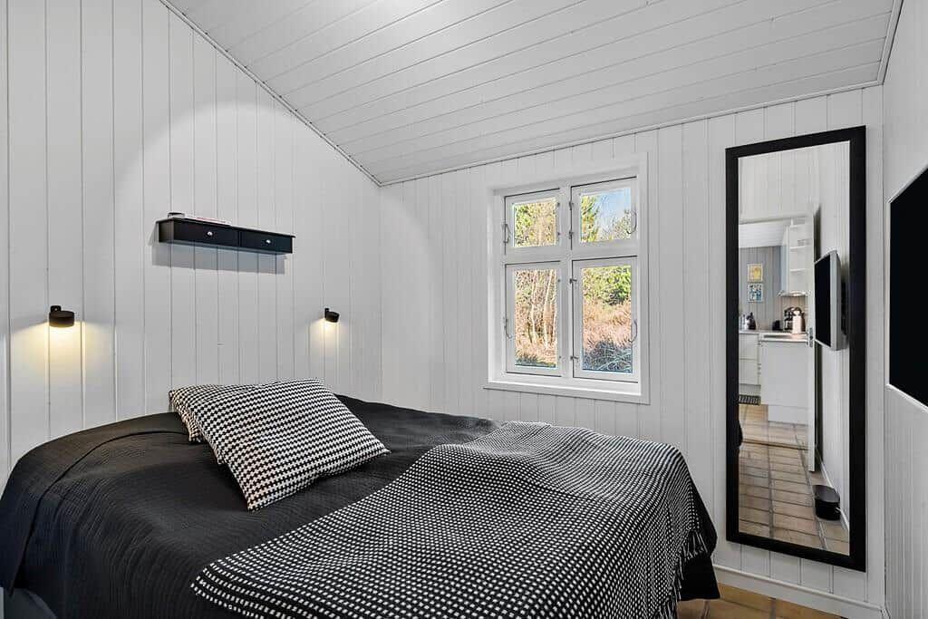 Schlafzimmer mit Bett, Fenster und Spiegel. Wände und Decke sind weiß verputzt.