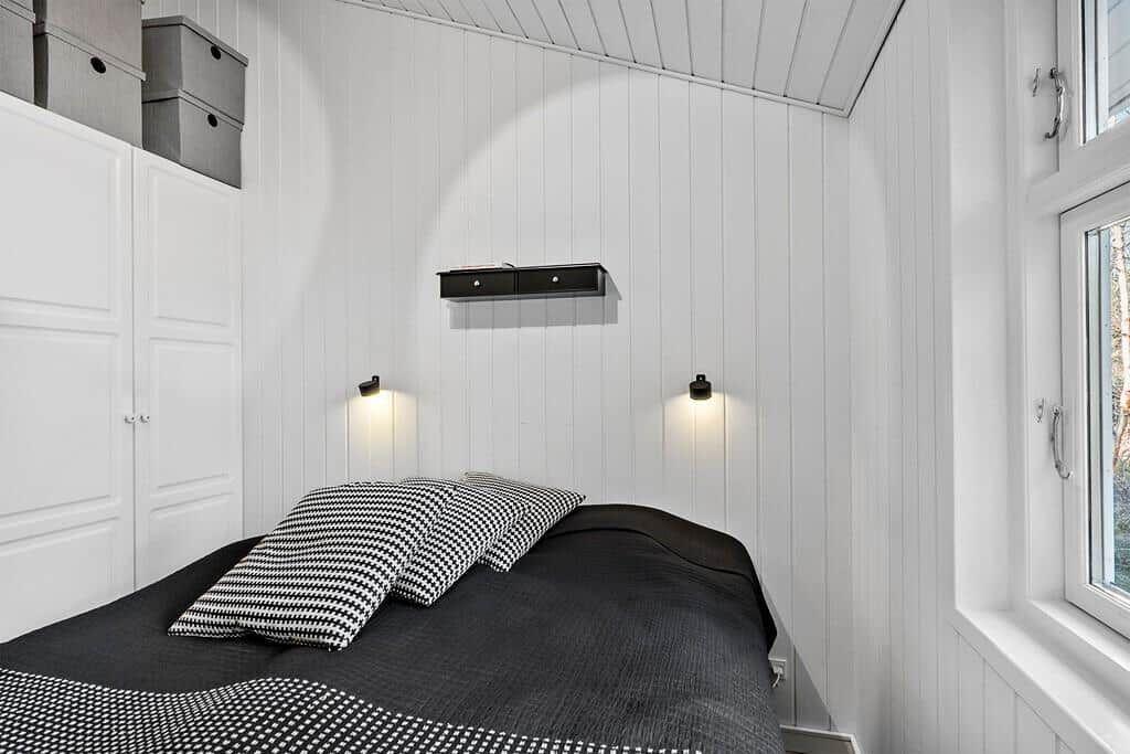 Schlafzimmer mit Bett, Schrank und Fenster. Wände sind weiß verkleidet.