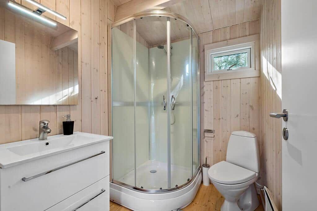 Badezimmer mit Dusche, Waschbecken und Toilette. Holzwände und Fenster.