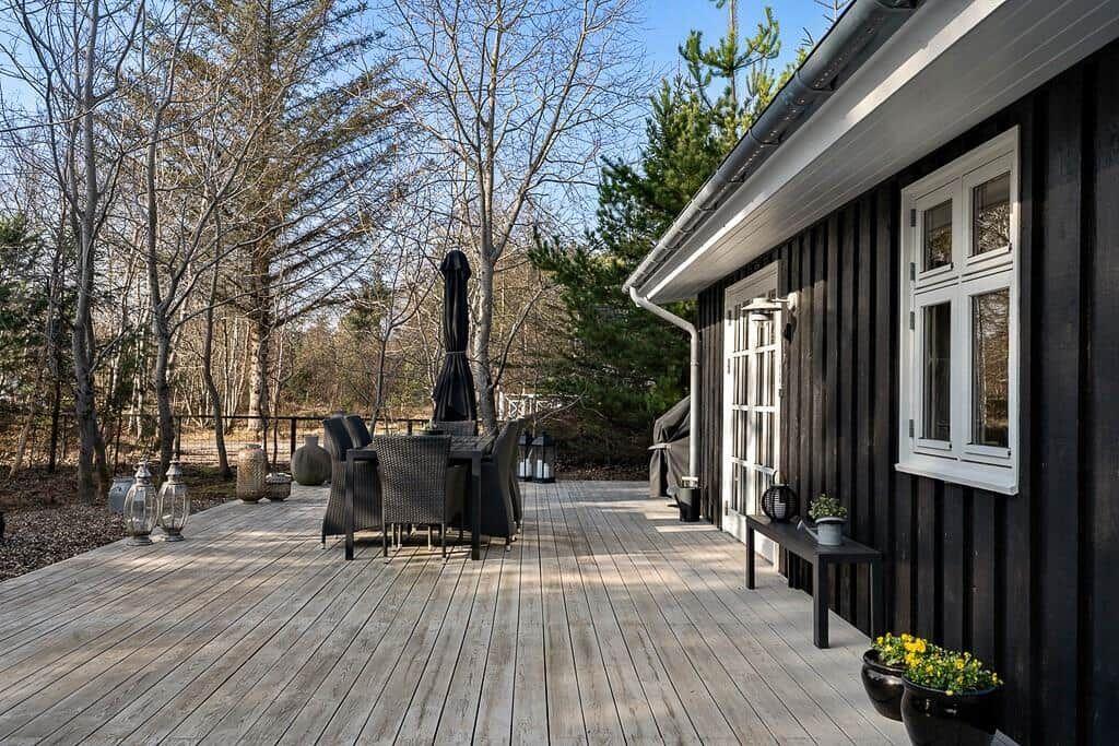 Terrasse mit Tisch, Stühlen und Sonnenschirm neben einem dunklen Holzhaus.