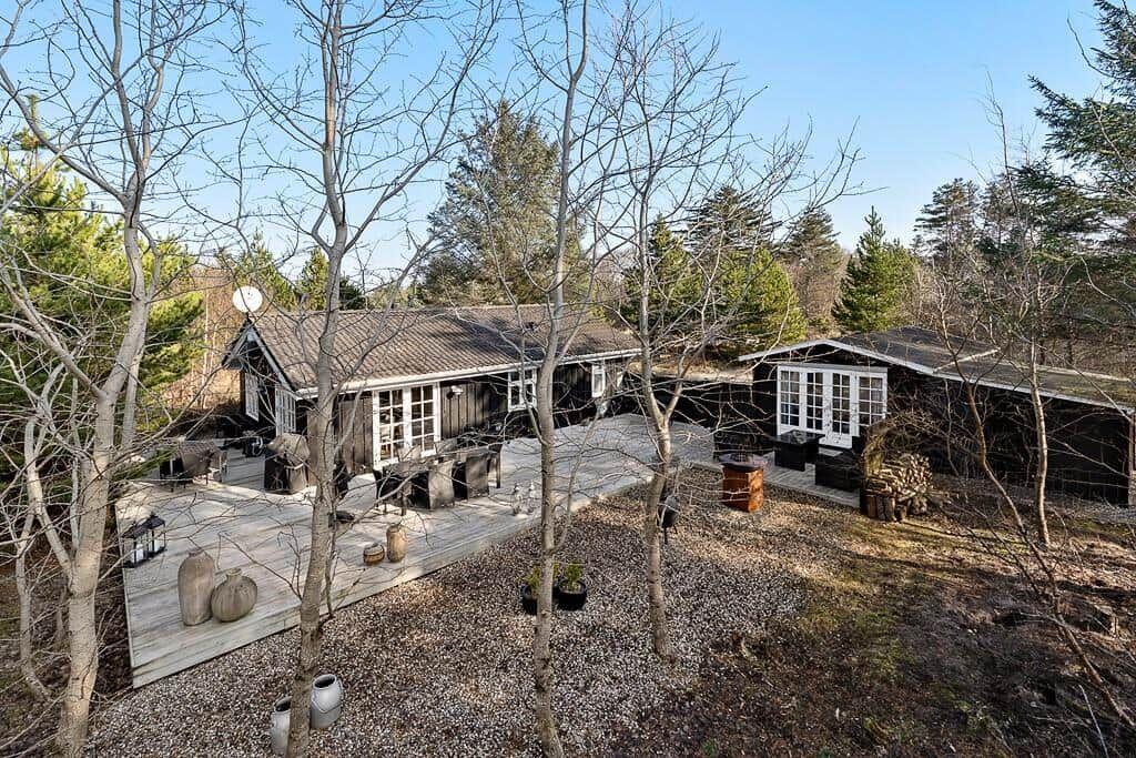 Holzhaus mit Terrasse und Garten. Umgeben von Bäumen und freiem Platz.