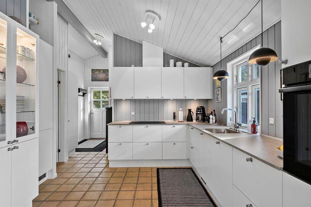 Moderne Küche mit weißen Schränken, Steinplatten und Fenster mit Blick nach draußen.