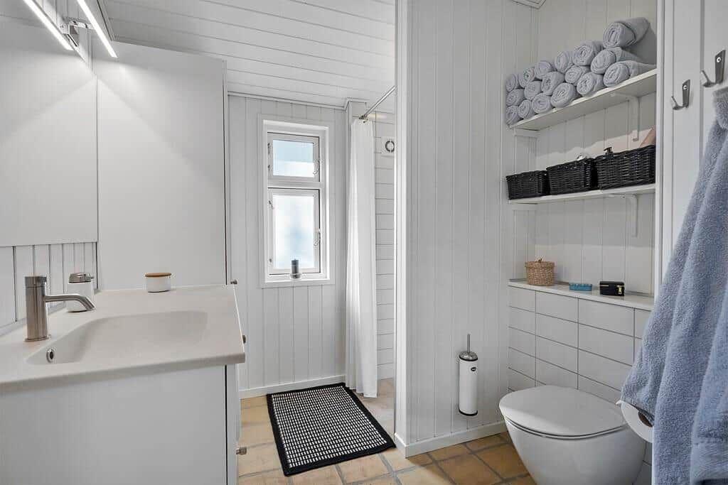 Badezimmer mit Waschbecken, Toilette, Dusche und Regalen mit Handtüchern.