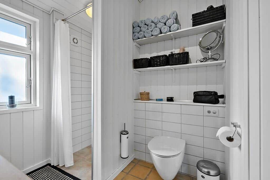 Badezimmer mit Dusche, Toilette und Regalen mit Handtüchern und Kosmetikartikeln.