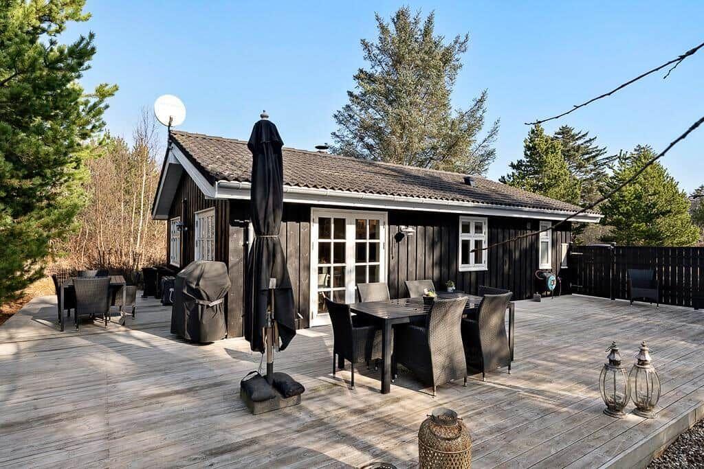 Holzhaus mit Terrasse, Tisch, Stühlen und Sonnenschirm. Umgeben von Bäumen und klarer Luft.