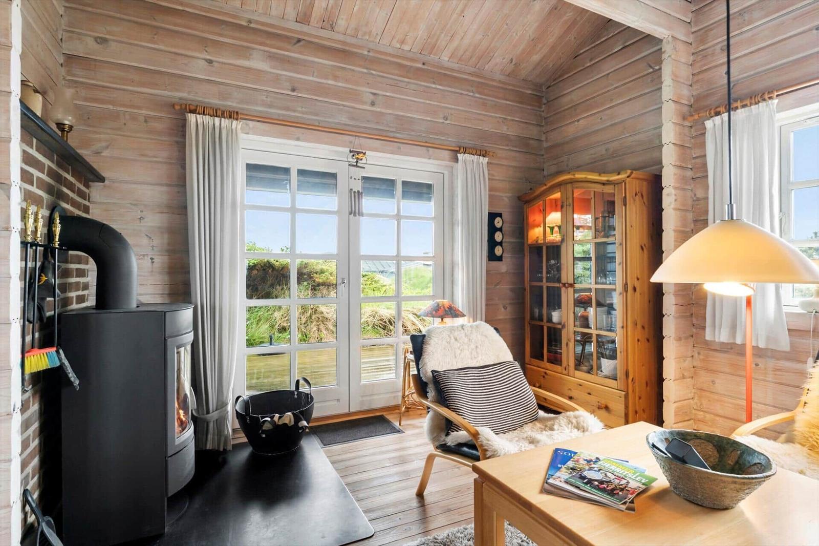 Wohnzimmer mit Holzwand, Kamin und Glasfront zum Garten.