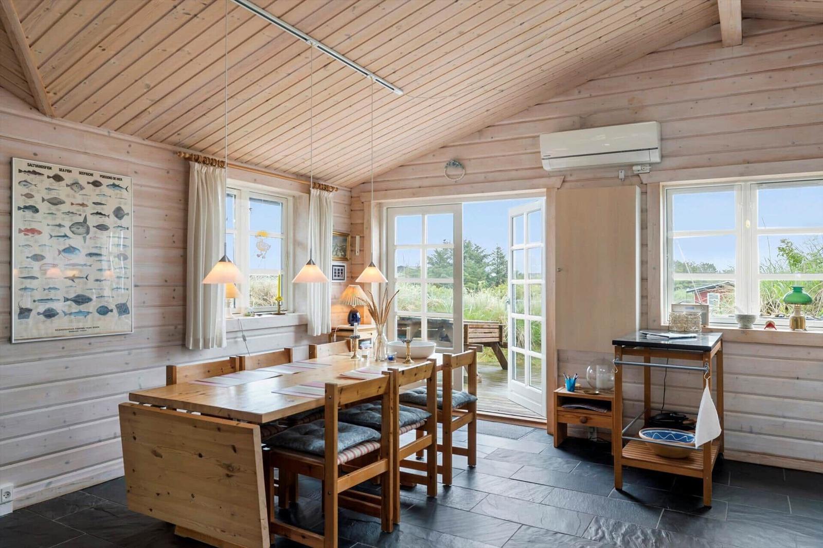 Esszimmer mit Holztisch, Stühlen und Fenstern. Wandbild mit Fischzeichnungen.