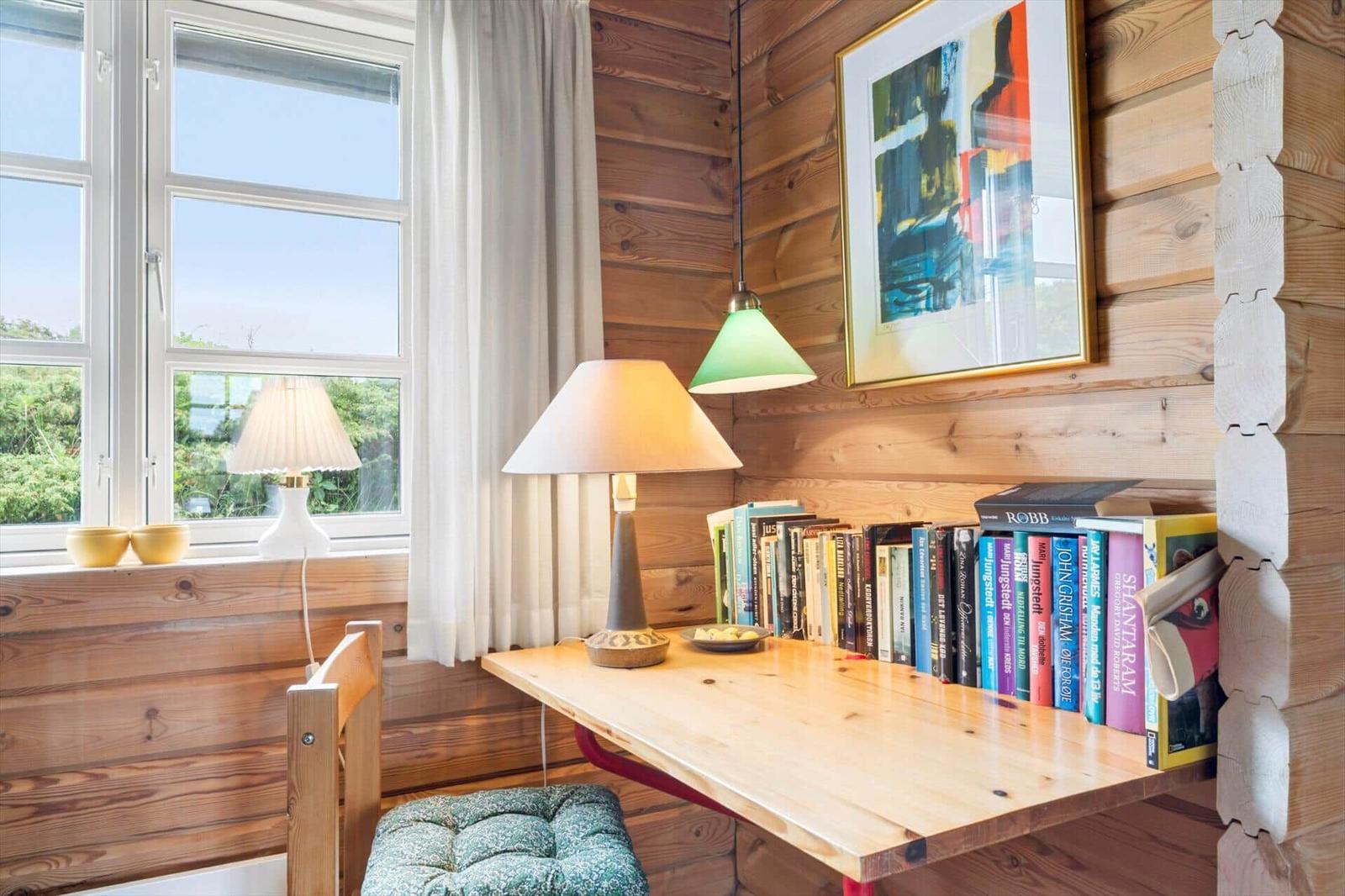 Holzgetäfelte Wand mit Schreibtisch, Lampe und Bücherregal. Fenster mit Blick auf Grün.