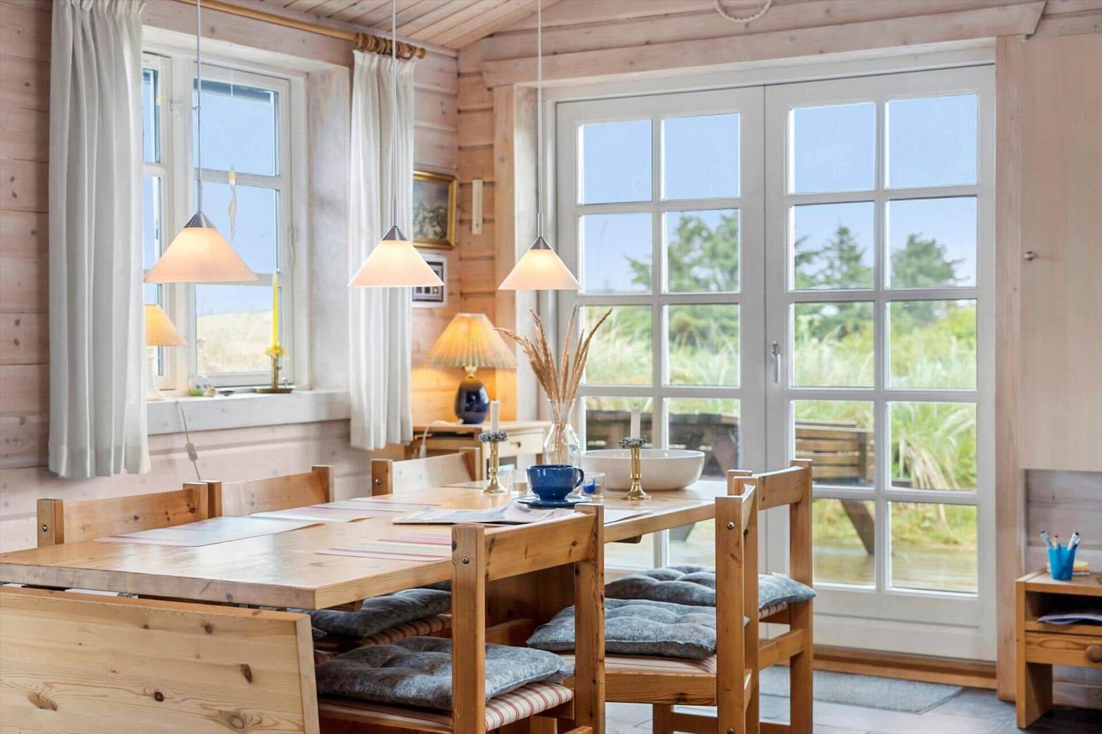 Esszimmer mit Holztisch, Stühlen und Blick auf Grünflächen.