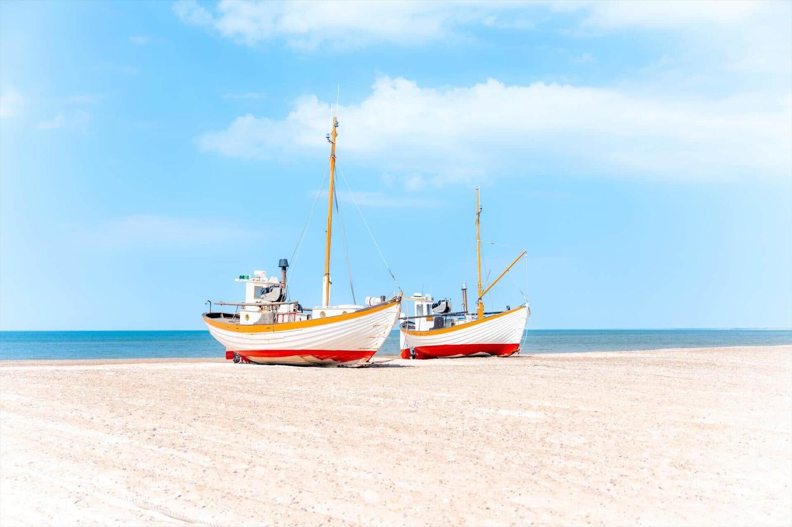 Zwei Fischerboote stehen auf dem Strand vor dem Meer unter blauem Himmel.