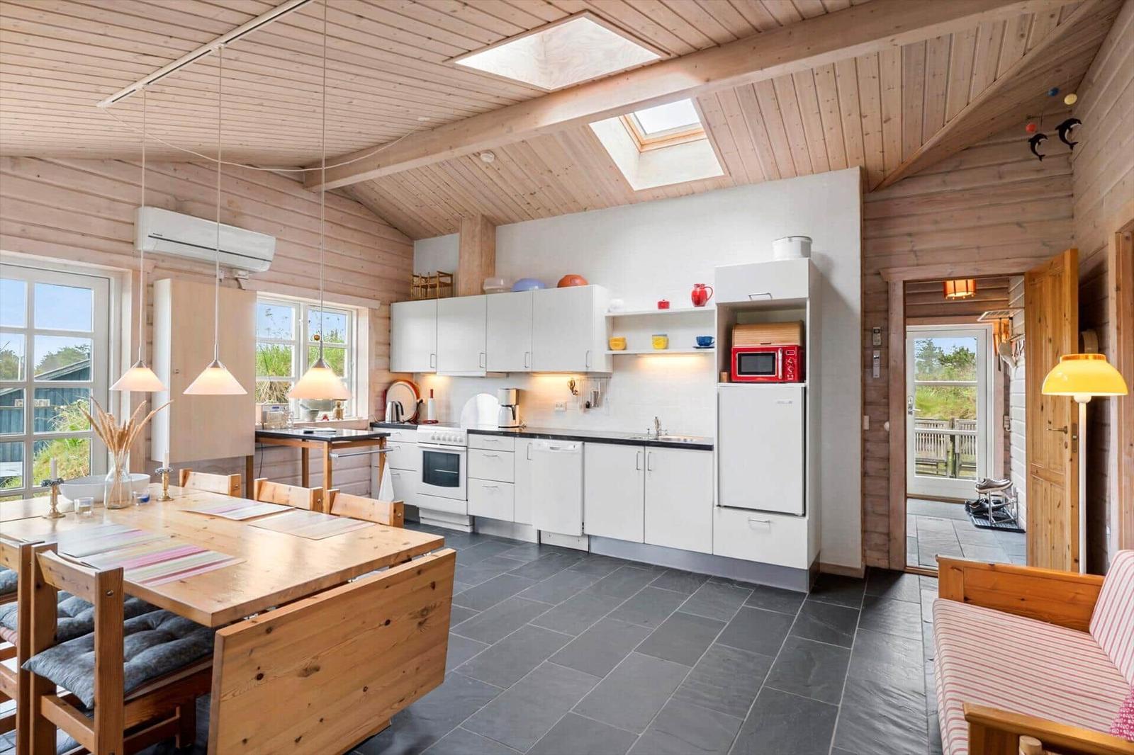 Küche mit Essbereich und Schlafzimmer im Hintergrund. Holzdecke, Fenster und Küchenzeile.