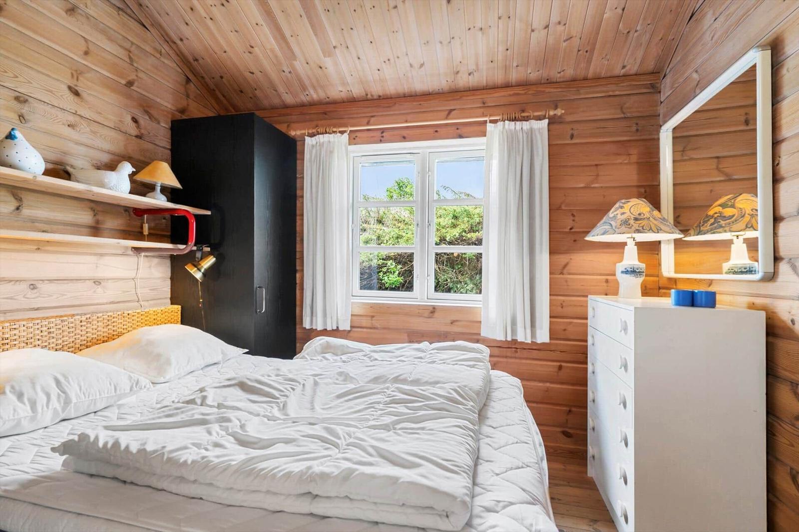 Schlafzimmer mit Holzwand, Bett, Schrank und Fenster mit Blick auf Grün.