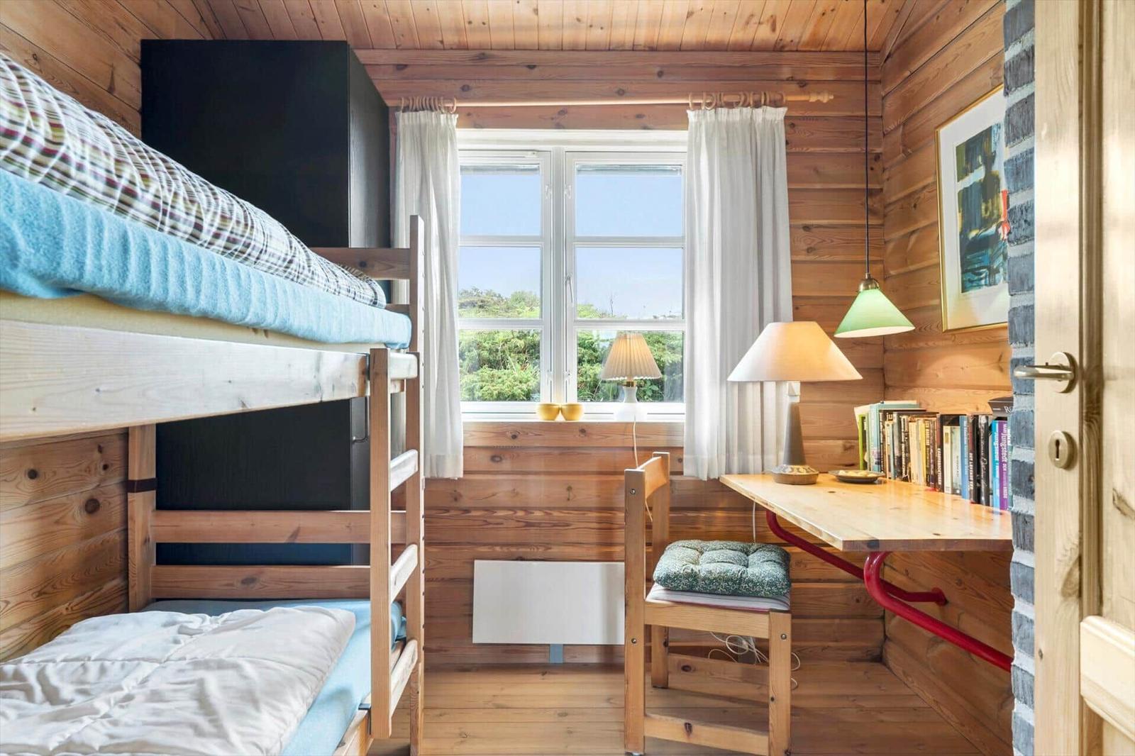 Zimmer mit Doppelstockbett, Schreibtisch und Fenster mit Blick auf Grün.