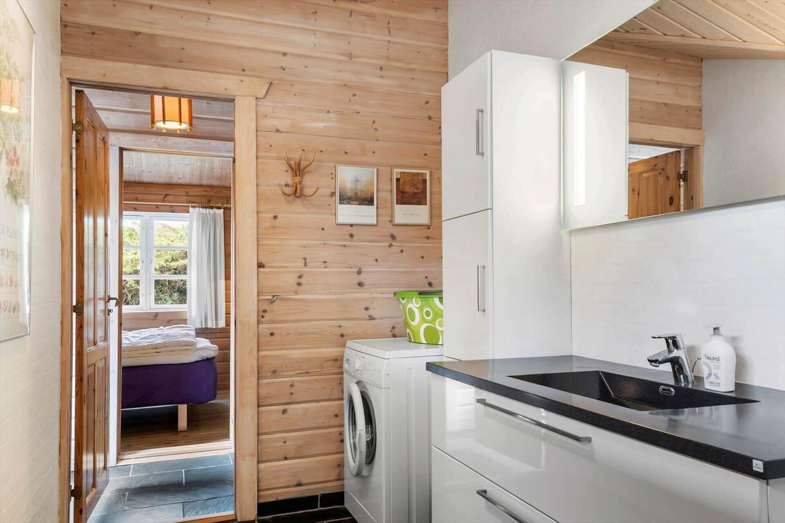 Küche mit Waschmaschine und Blick in Schlafzimmer mit Bett und Fenster.
