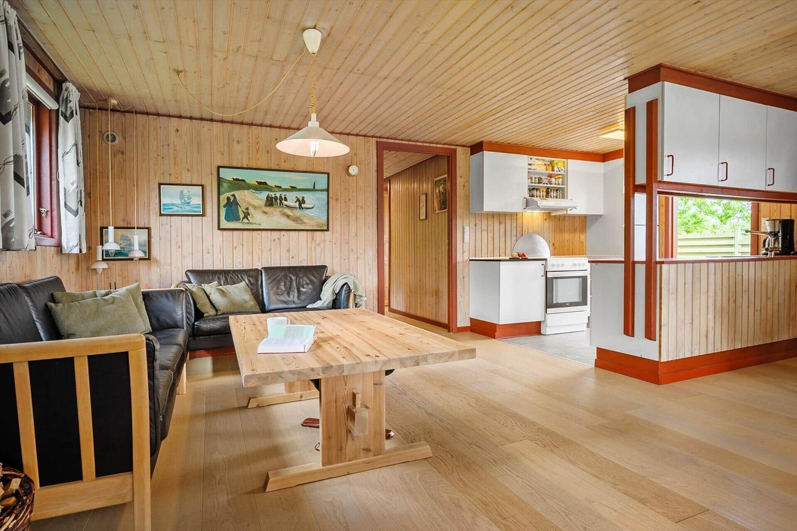 Wohn- und Küchenbereich mit Holzdecke, Sofa, Tisch und weißen Küchenmöbeln.