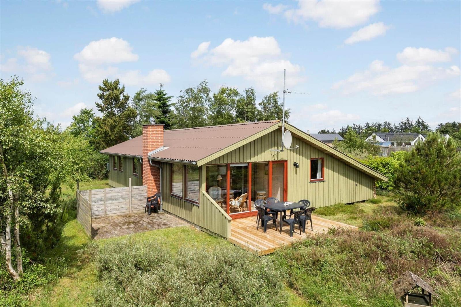 Grünes Ferienhaus mit Terrasse und Garten. Sicht auf Wohnbereich und Grillplatz.