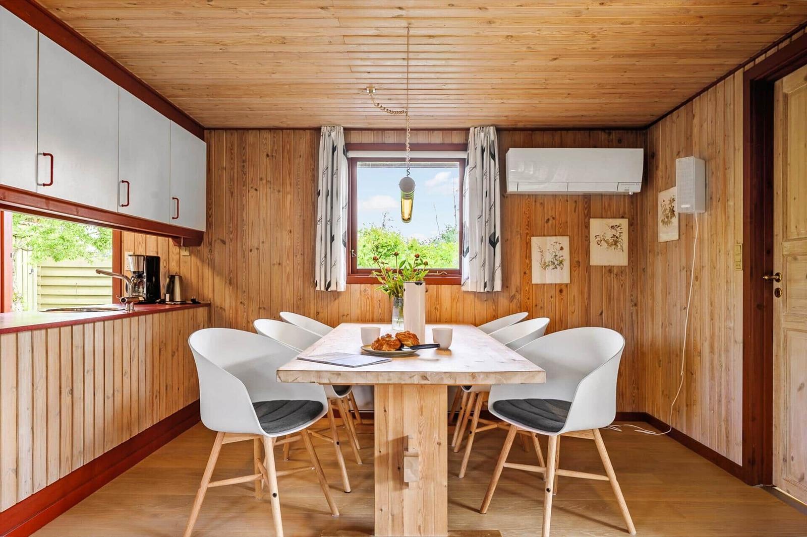 Essbereich mit Holztisch, weißen Stühlen und Fenster mit Blick auf Grün.