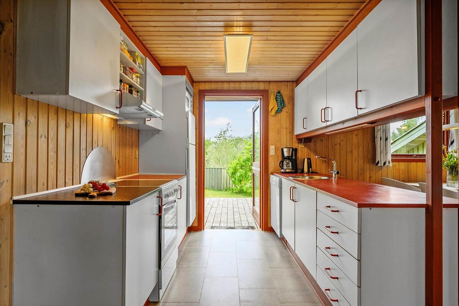 Küche mit weißen Schränken, Holzwänden und Blick auf die Terrasse.