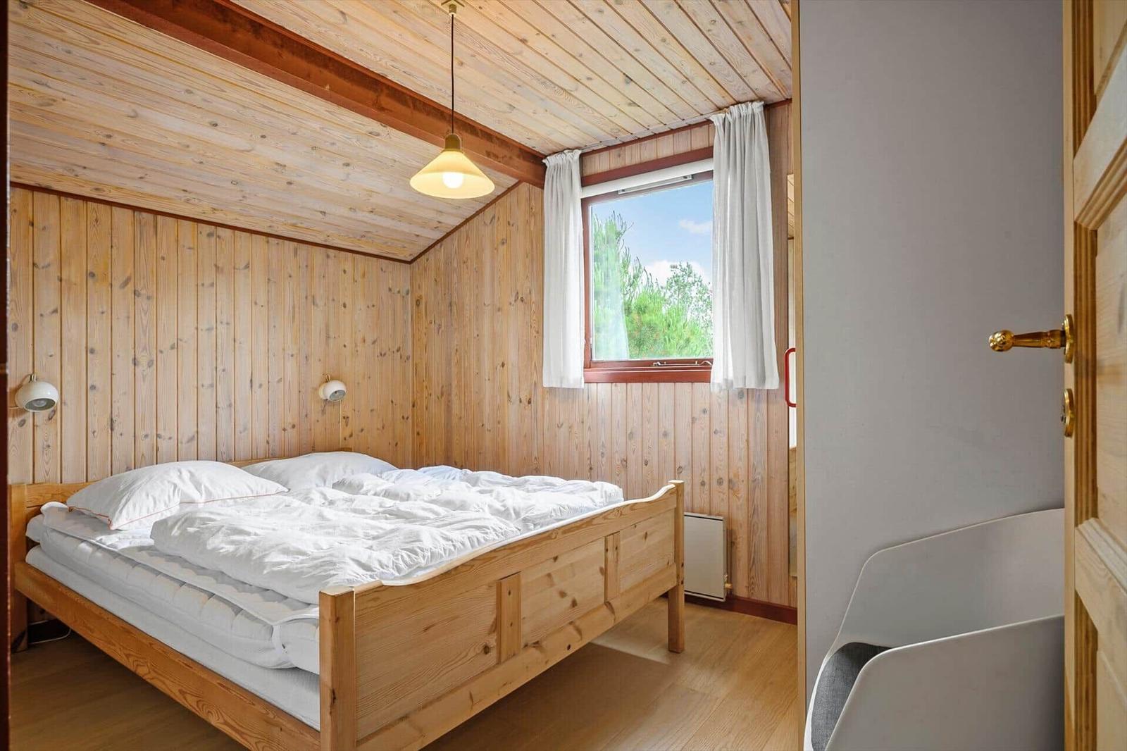 Schlafzimmer mit Holzwand, Bett und Fenster mit Blick auf Grün.