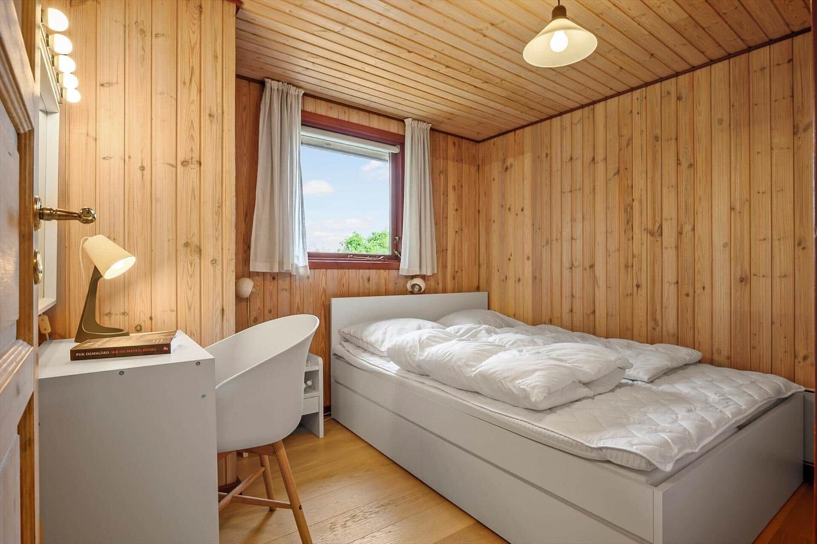 Schlafzimmer mit Holzwänden, weißem Bett und Schreibtisch mit Stuhl.