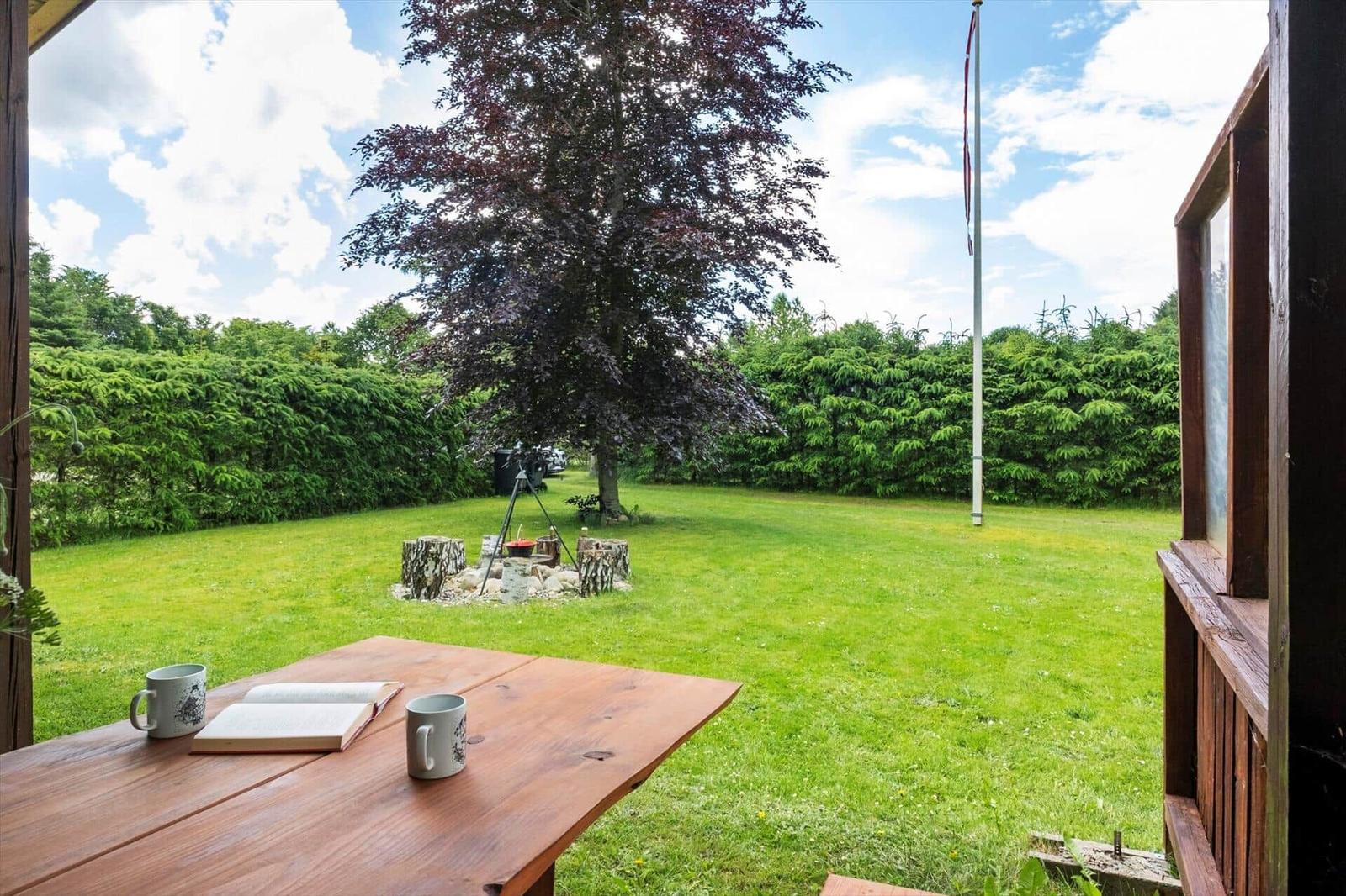 Von der Terrasse aus blickt man auf einen grünen Garten mit einem Baum und einem Grillplatz.