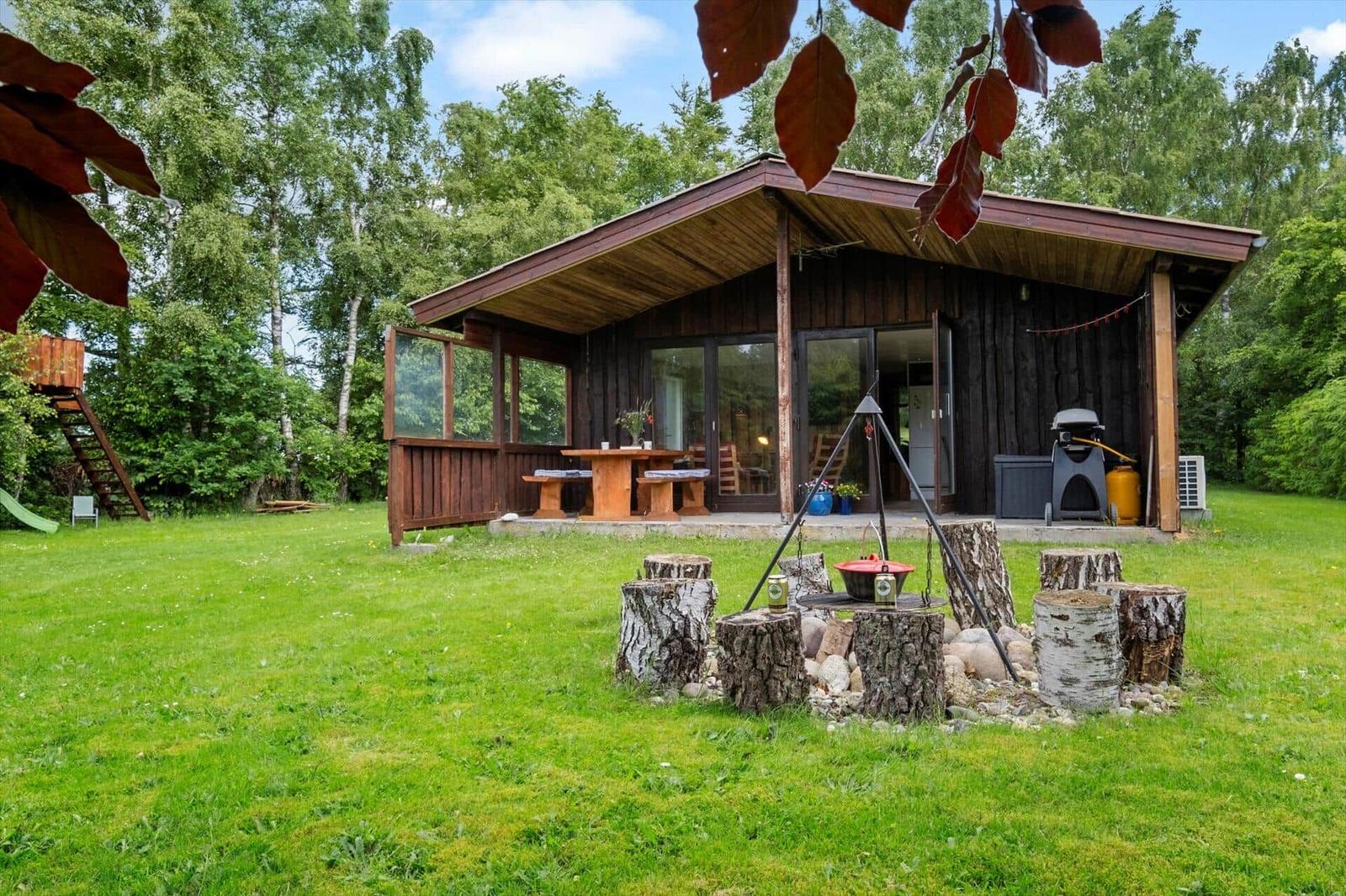 Holzhütte mit Terrasse, Grill und rustikalem Grillplatz im Grünen.