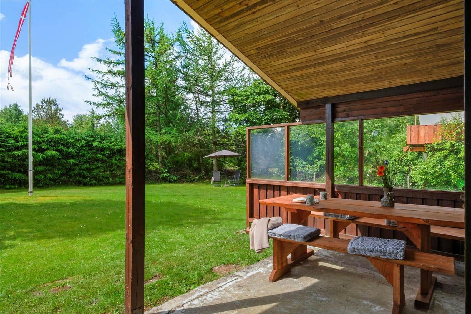 Holzterrasse mit Tisch und Bänken, Blick auf grünen Rasen und Wald.