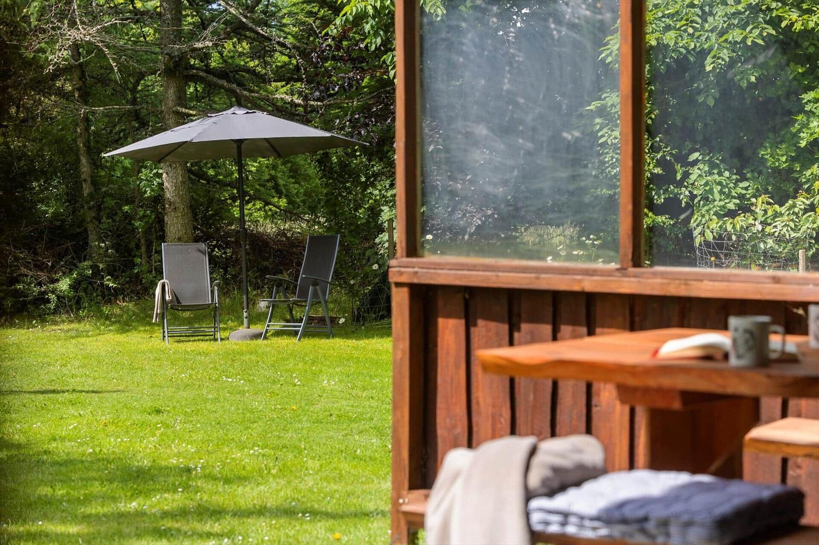 Terrasse mit Holztisch und Blick auf grünen Garten mit Sonnenschirm und Liegestühlen.