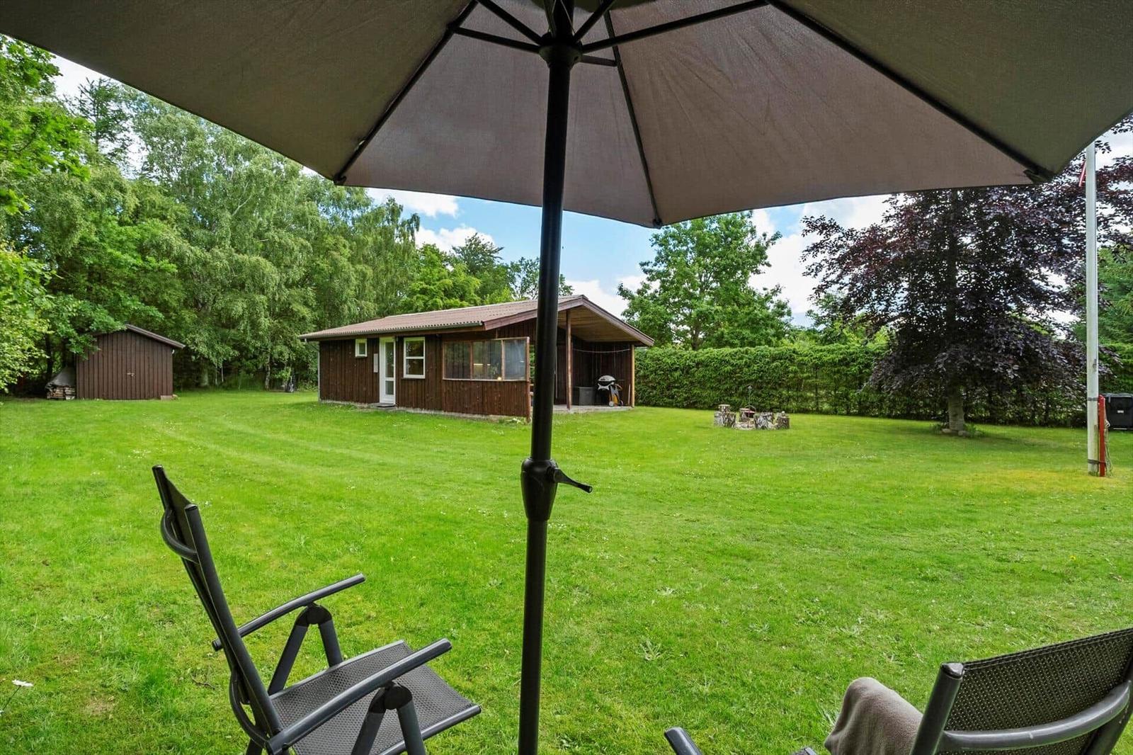 Großer Garten mit Liegestühlen und Sonnenschirm. Im Hintergrund steht eine Holzhütte.