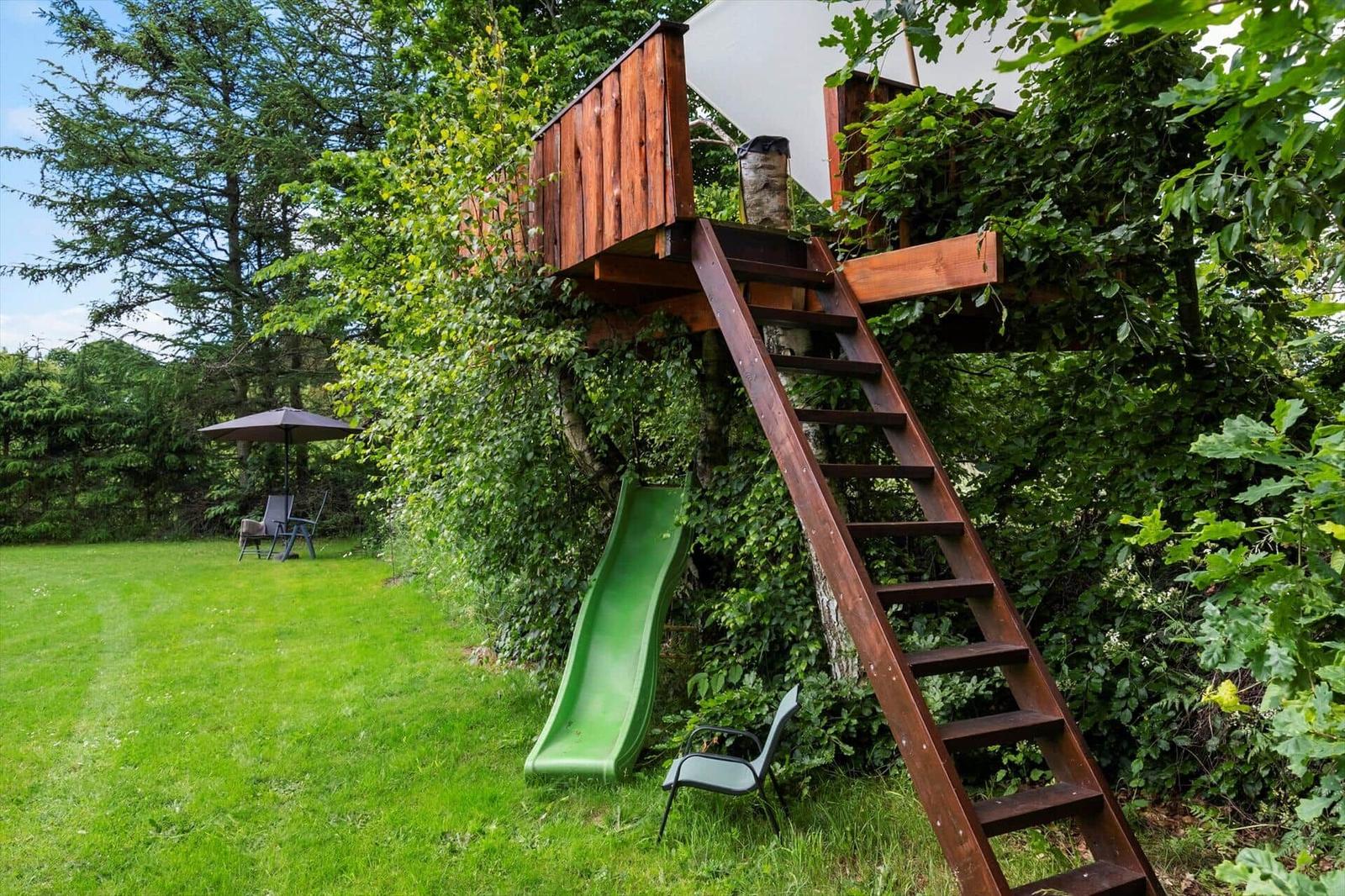 Holzhaus im Baum mit Leiter und grünem Rutschhang im Garten